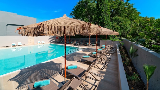 A poolside area with lounge chairs, a pool, and a thatched umbrella. - Amphitryon City Hotel (Rhodes)