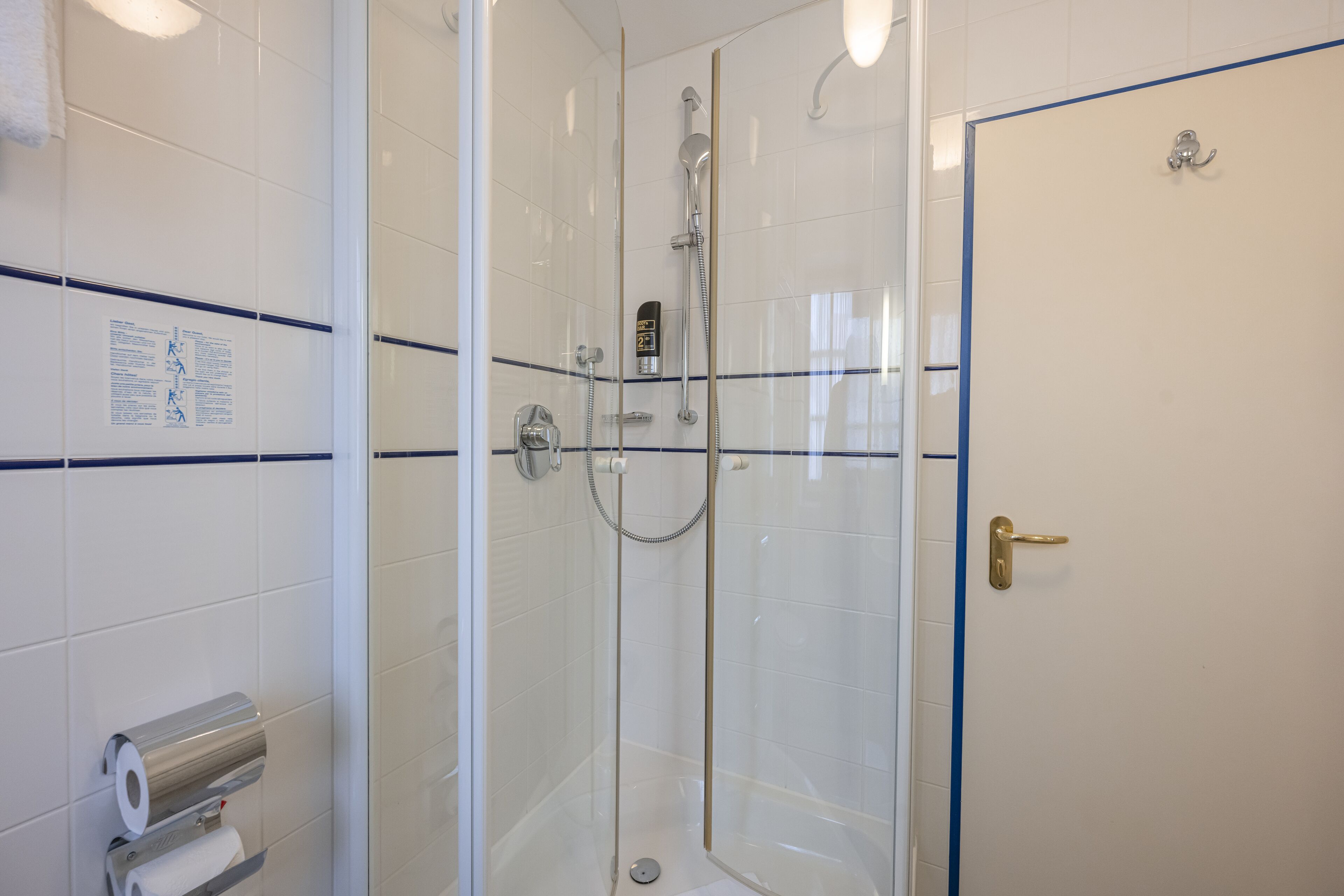 A glass-enclosed shower with a handheld showerhead and a wall-mounted control panel.