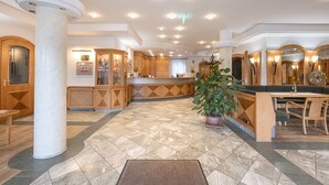 A spacious hotel lobby with a marble floor, wooden reception desk, and a large potted plant. - Hotel Neuwirt (Sauerlach)
