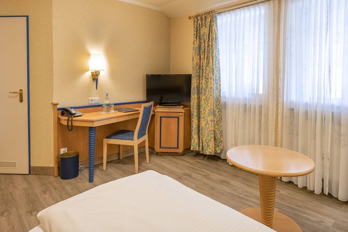 Una habitación de hotel con una cama, un escritorio con una silla, un televisor y una mesita.