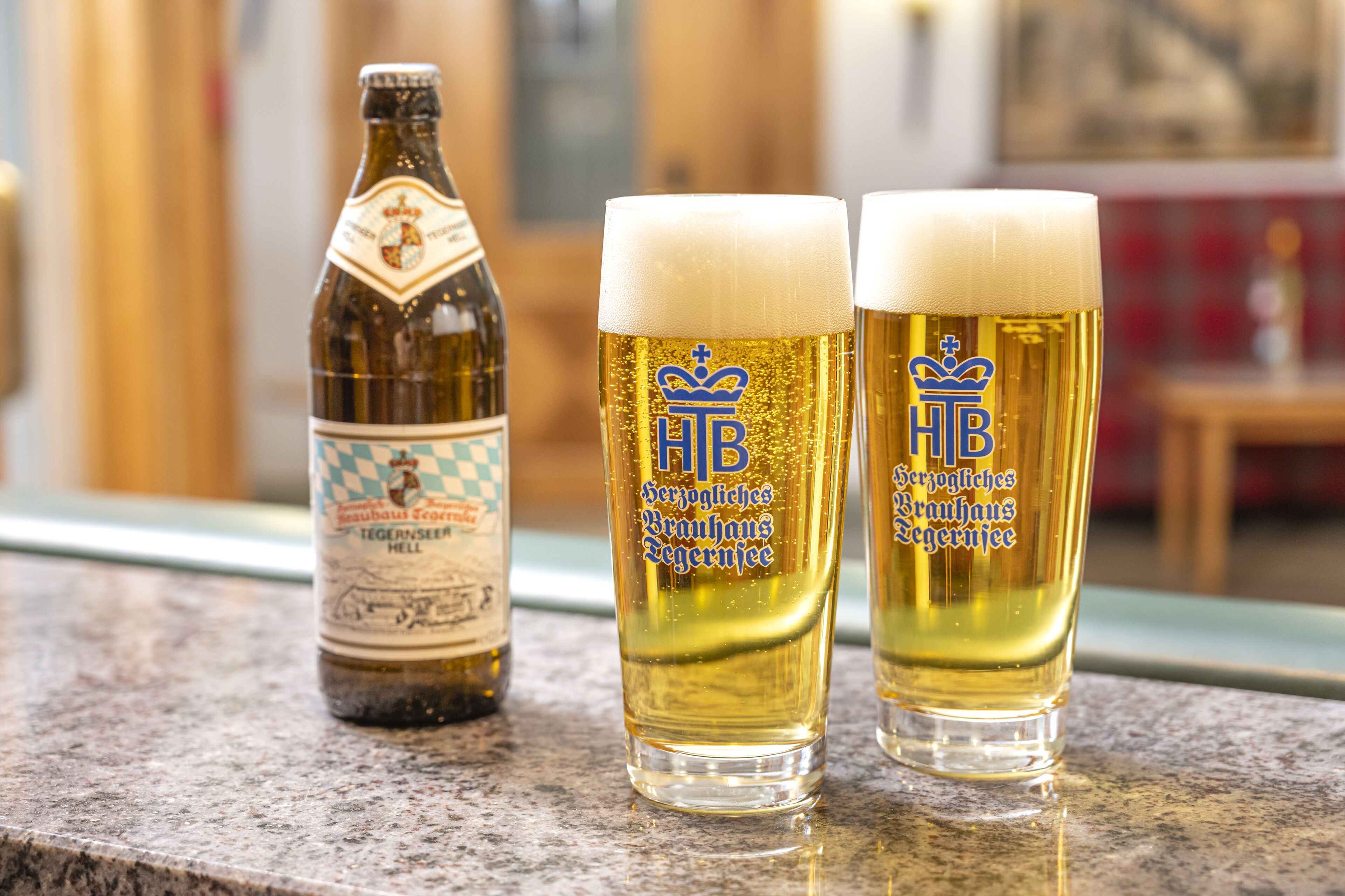 Una botella y dos vasos de cerveza con un logotipo, sobre una encimera.