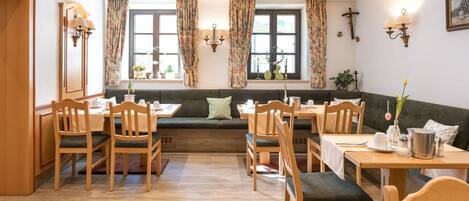 Un espace repas avec des tables et des chaises en bois, un banc et une fenêtre avec des rideaux.