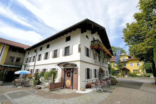 A traditional European building with a courtyard, a covered entrance, and outdoor seating. - Hotel Neuwirt (Sauerlach)