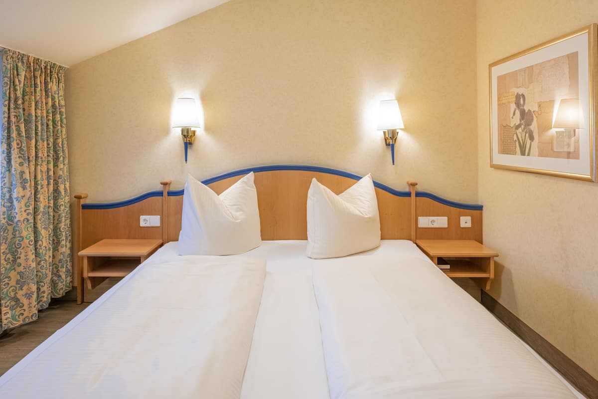 Una cama doble con dos mesitas de noche, cada una con una lámpara, en una habitación de hotel con una pared lisa y un cuadro enmarcado.