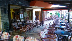 An outdoor cafe with wicker furniture and a glass wall overlooking a street. - Katerini Hotel Apartments (Rethymno)