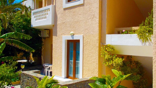 A modern two-story building with a balcony, a small patio area, and lush greenery in the foreground. - Katerini Hotel Apartments (Rethymno)