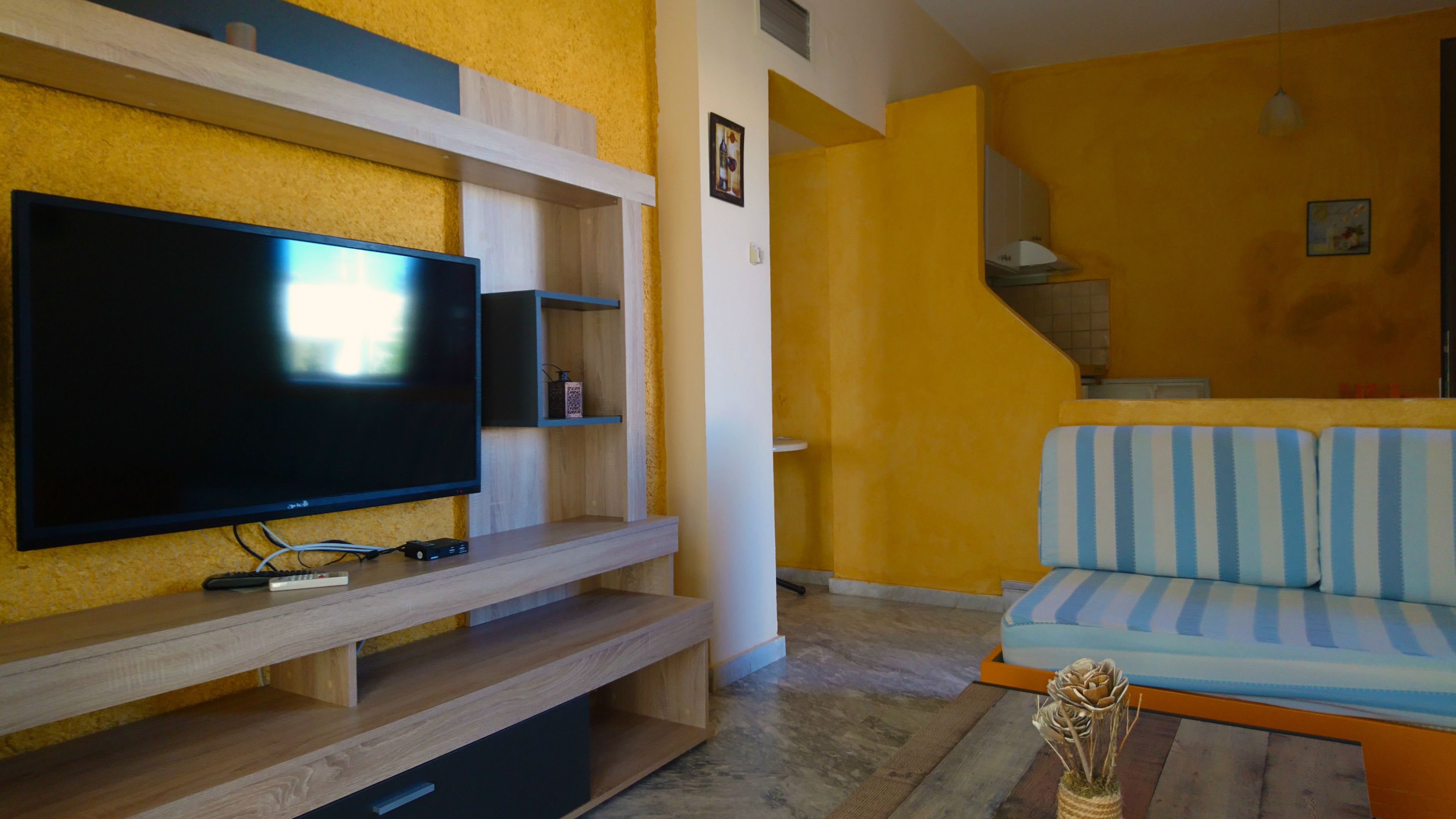 A living room with a flat-screen TV on a wooden stand, a striped sofa, and a staircase leading to an upper level.