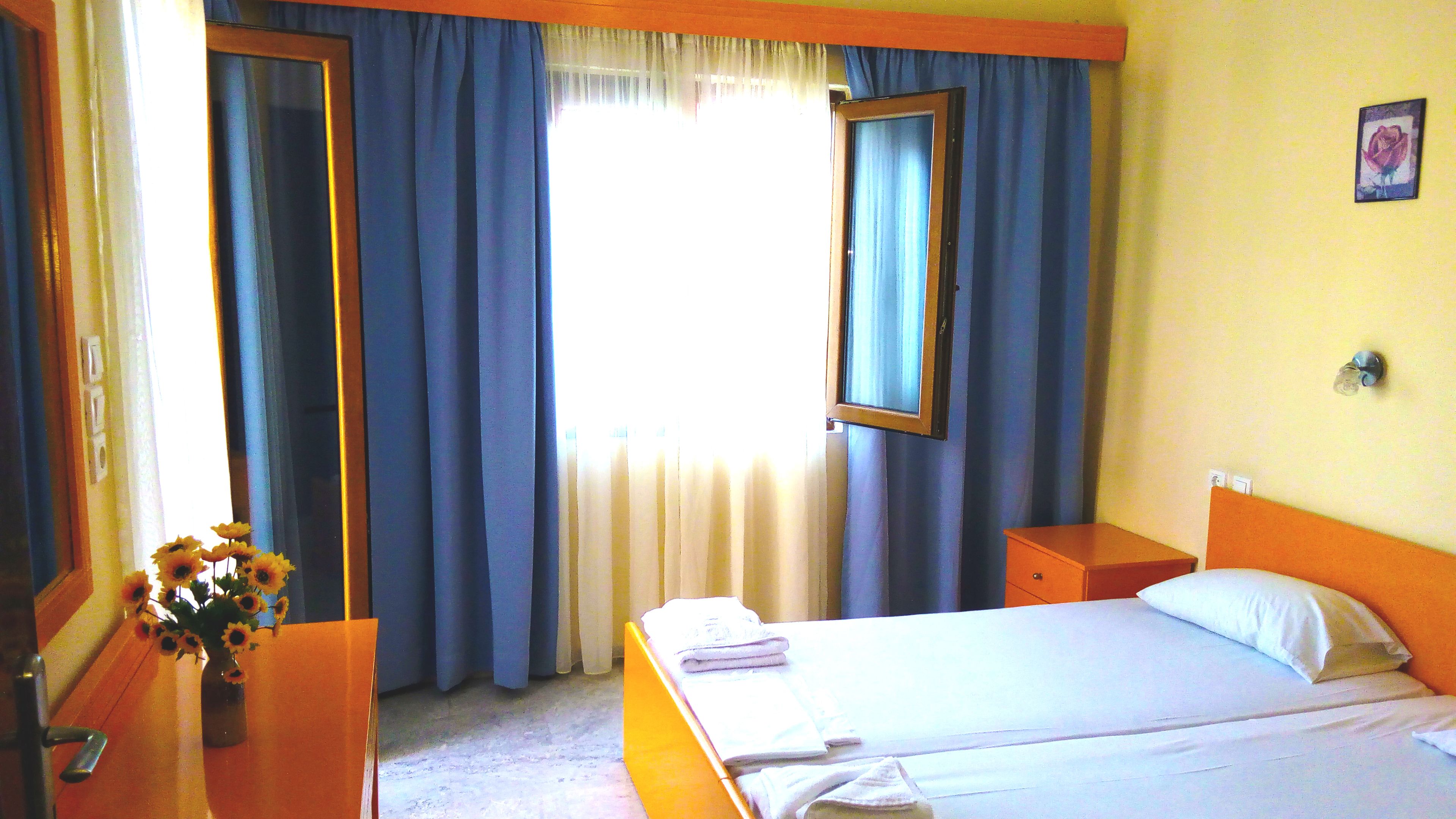 A hotel room with a bed, a nightstand, a dresser, and a window with curtains.