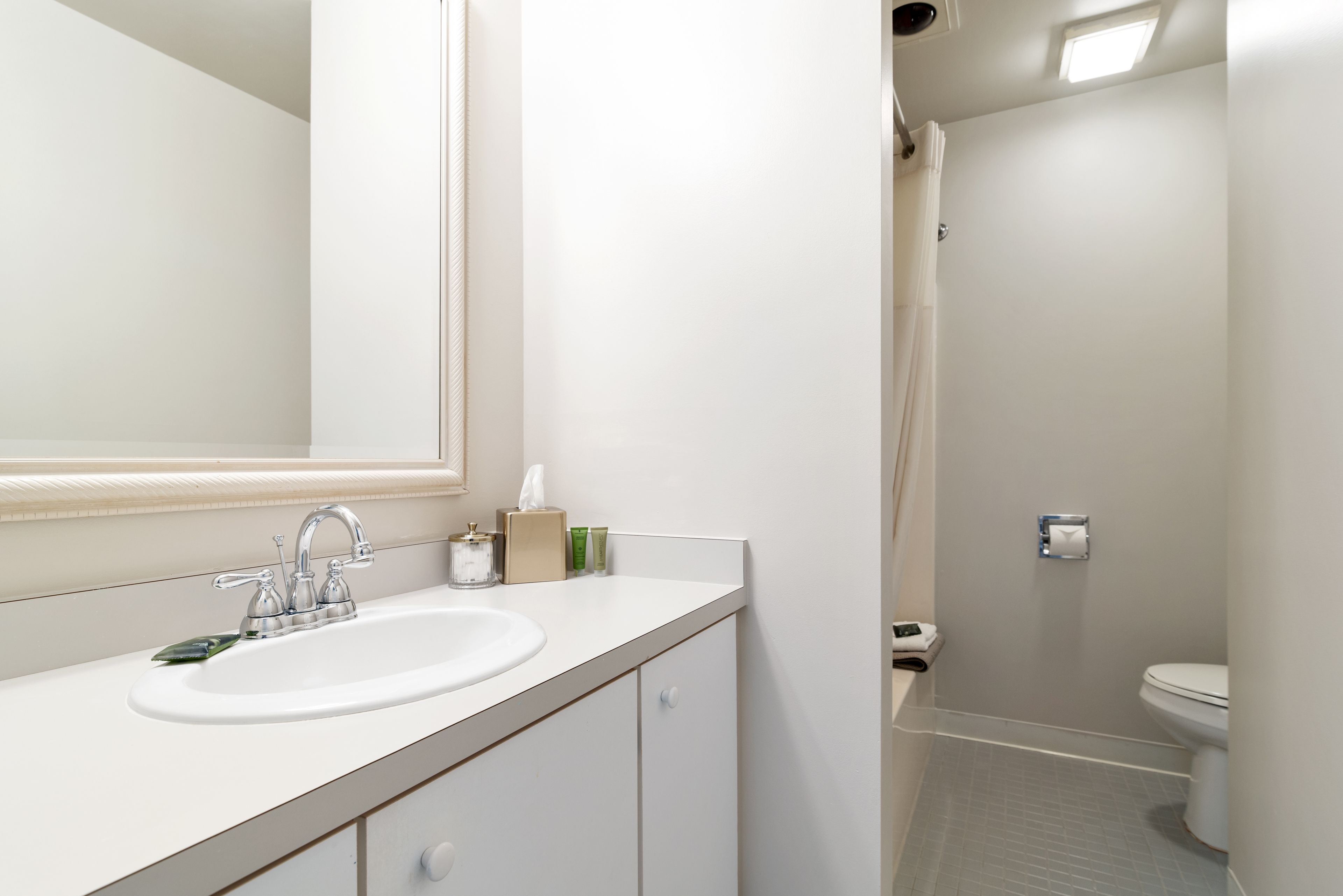 Et badeværelse med hvid vask, spejl og toilet.