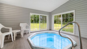 Una piscina exterior cubierta con un jacuzzi, rodeada de sillas de plástico blancas, ventanas amplias y una terraza de madera.