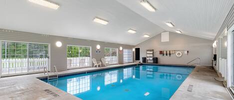Una piscina interior con agua azul cristalina, un suelo de baldosas y un techo blanco con luces fluorescentes.