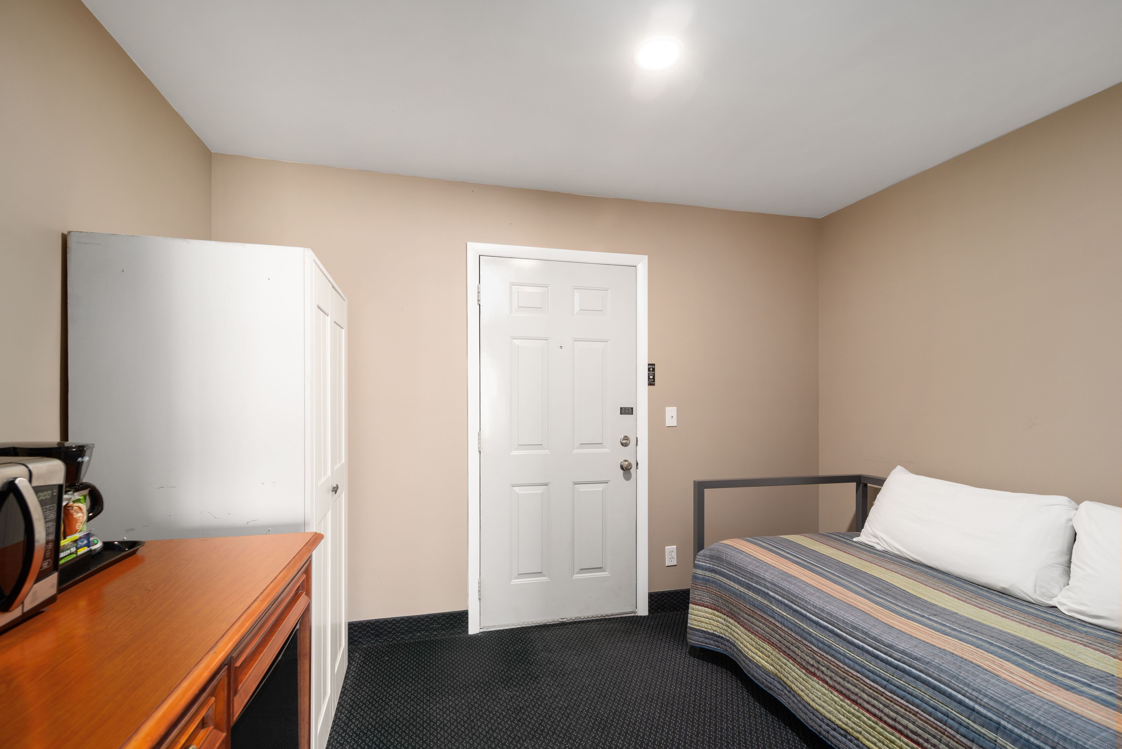 Una habitación de hotel con una cama, un aparador de madera, un microondas y una puerta blanca.