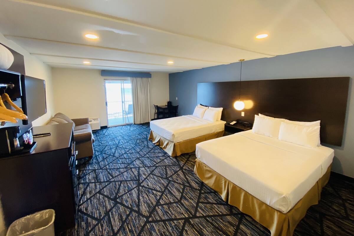 A hotel room with two beds, a desk, a chair, a TV, and a large window.