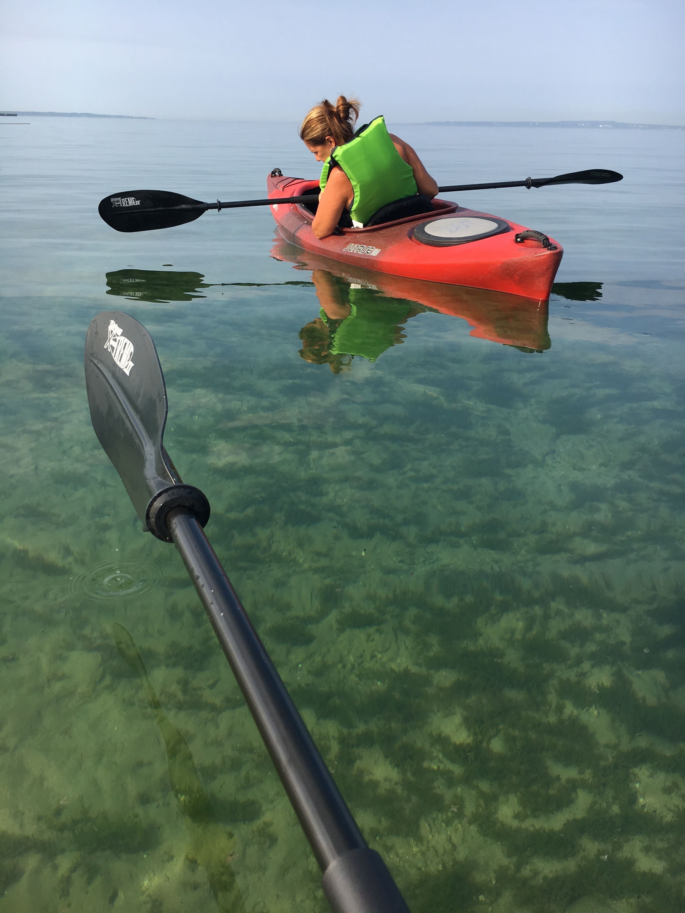 A kayak on calm water with a paddle in the foreground.