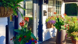 Entrada de un edificio con puerta de vidrio, plantas en macetas con flores y un buzón.