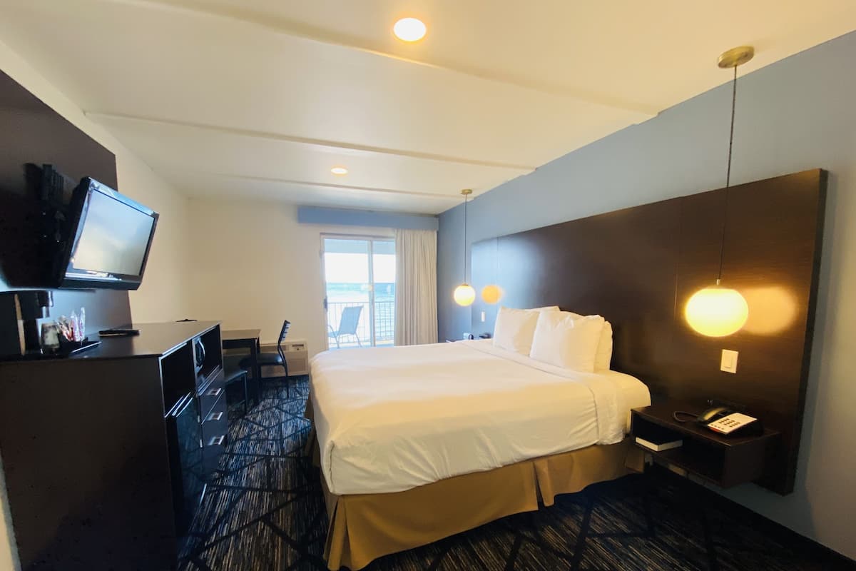 A hotel room with a large bed, a desk with a television, and a desk lamp.