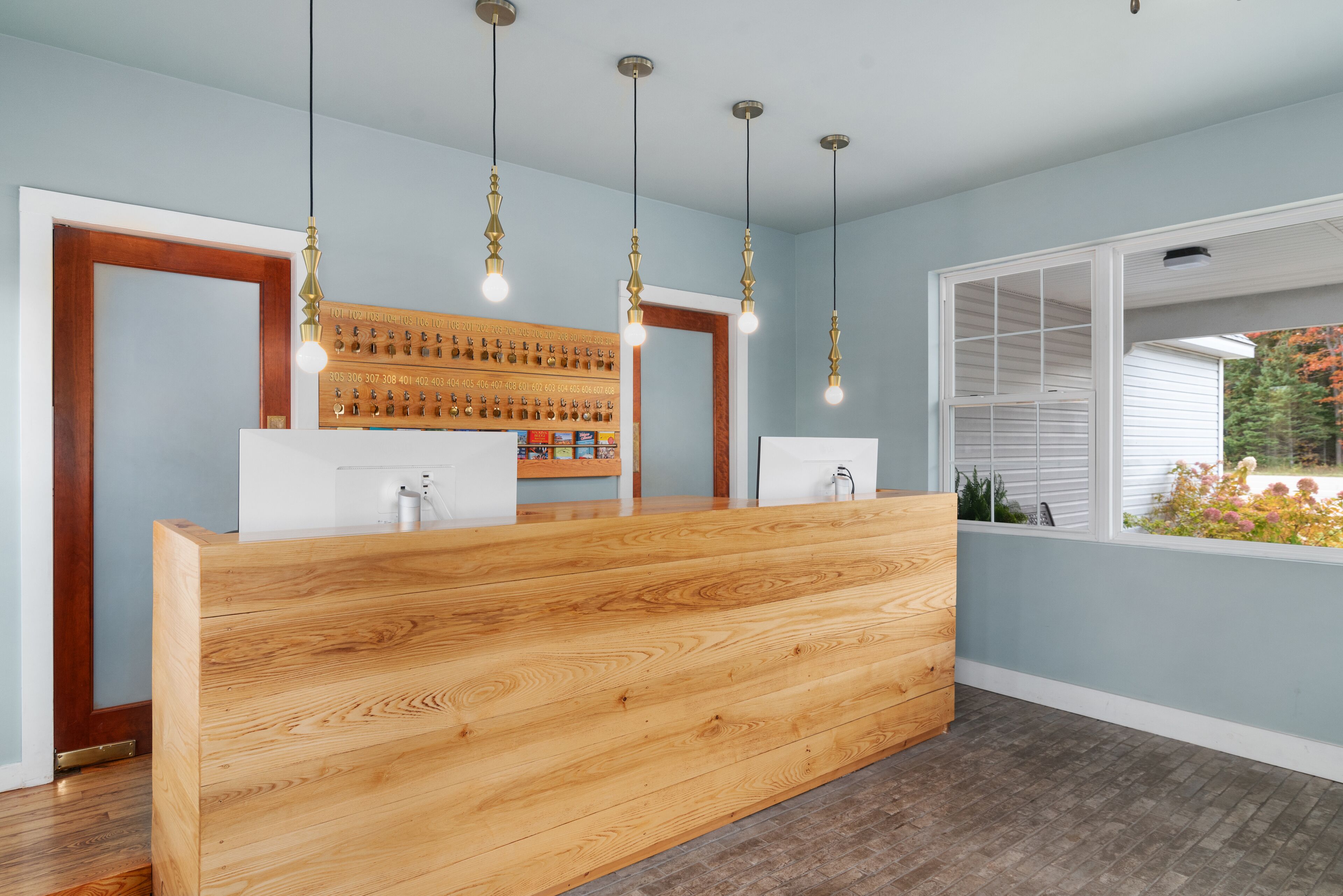 A reception desk with a wooden finish, three pendant lights, and a view of the outdoors through a window.