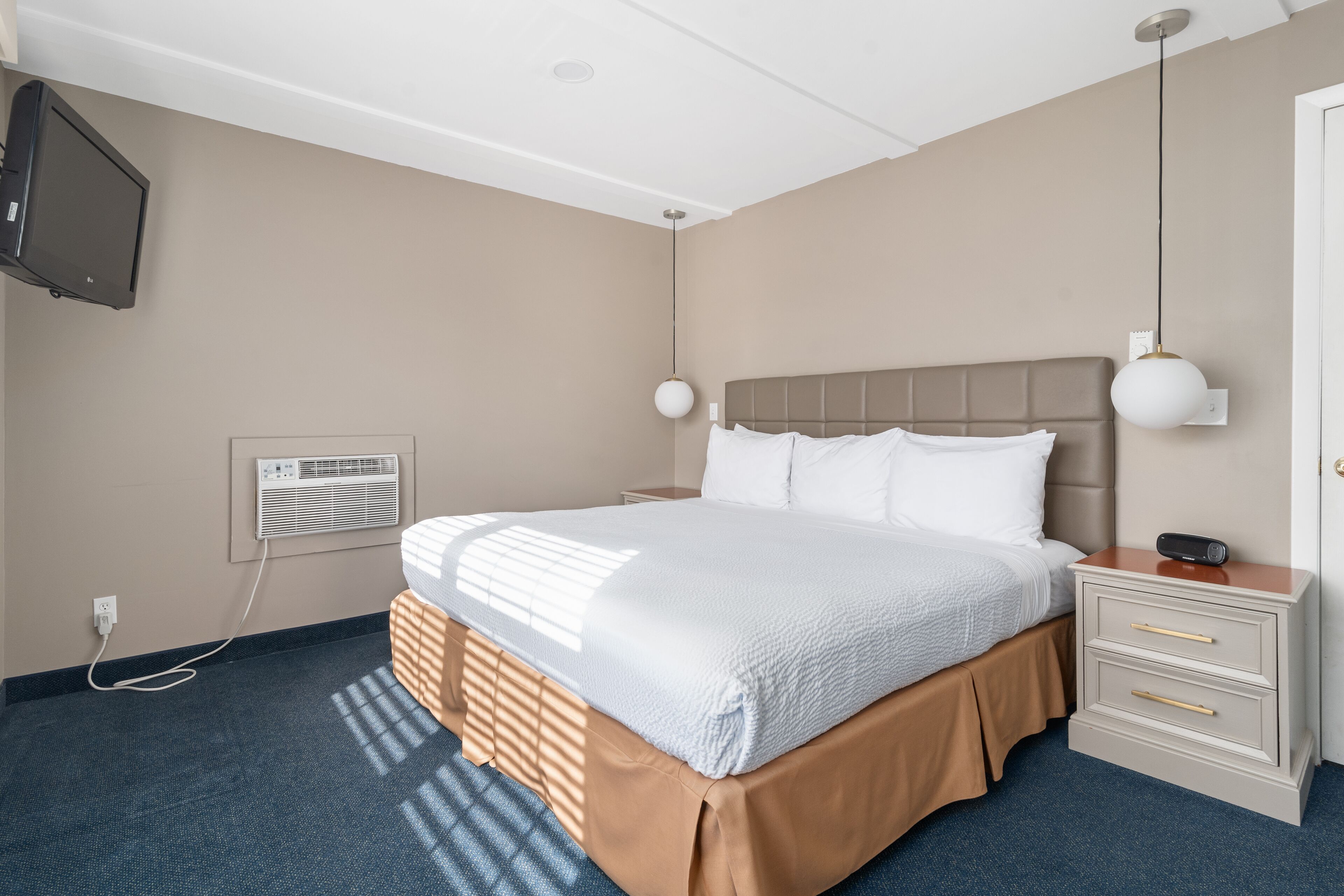 A hotel room with a bed, bedside tables, a TV, and a wall-mounted air conditioner.