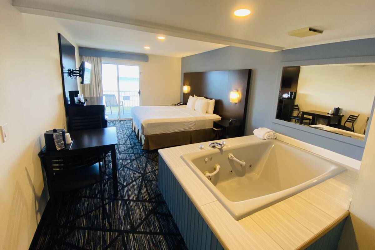A hotel room with a large bed, a separate bedroom, a bathroom with a bathtub, a desk, and a chair.