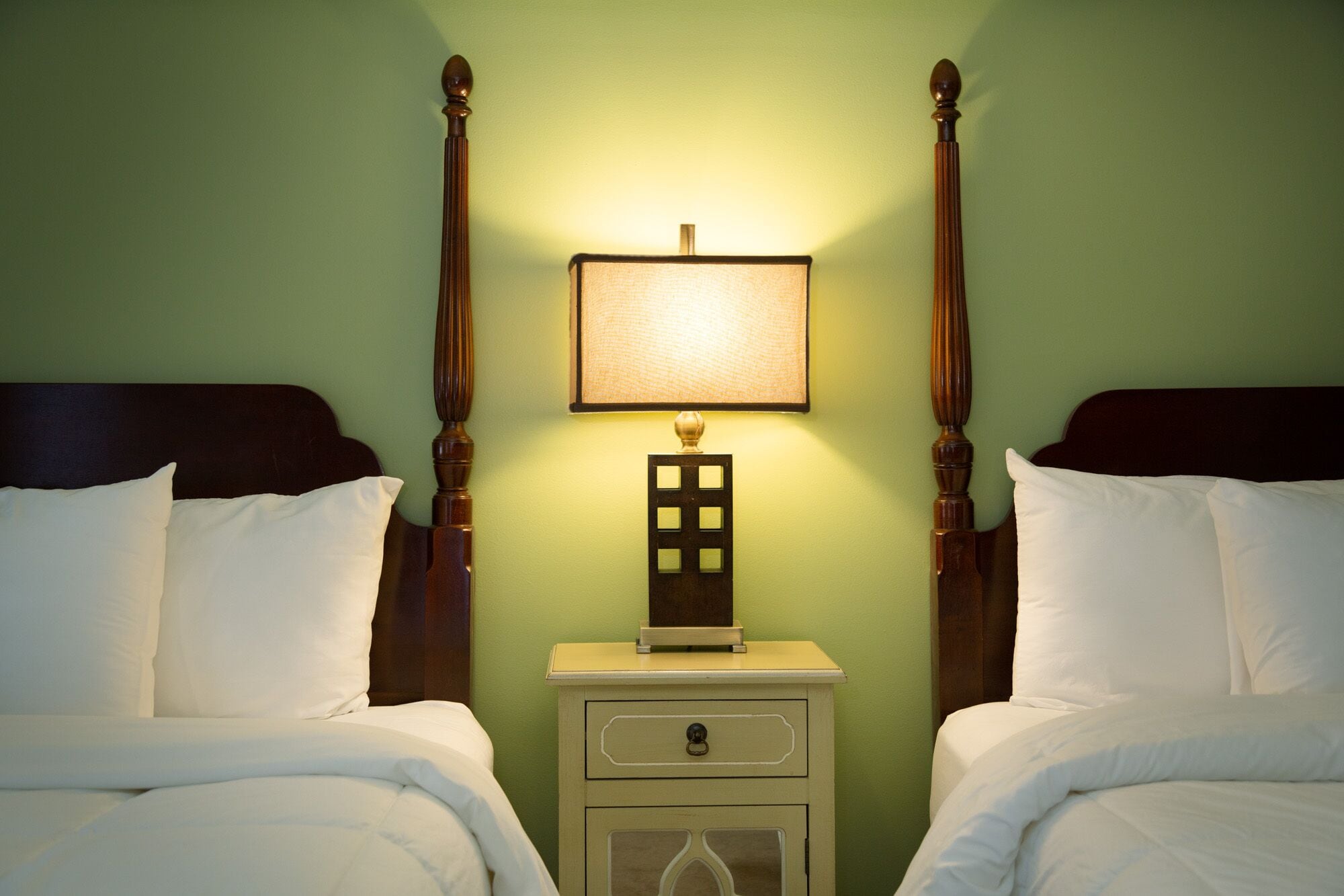 A room with two beds, a nightstand with a lamp, and a wall-mounted light fixture.