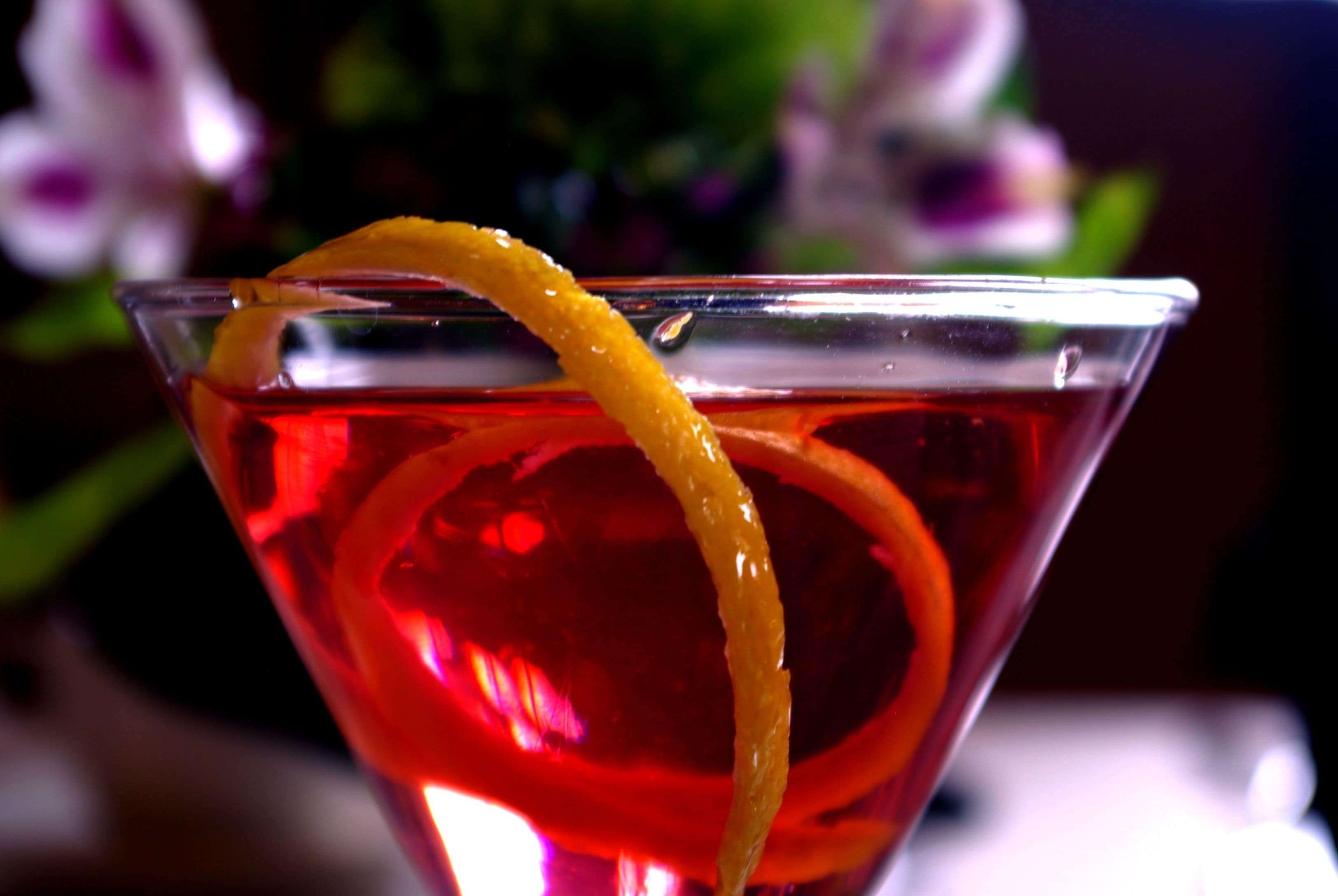 Een martini glas met een rode vloeistof en een sinaasappelschijfje.