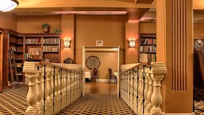 A grand staircase with ornate balustrades, a library with bookshelves, and a decorative wall with a framed map. - Grant Hall Hotel (Moose Jaw)