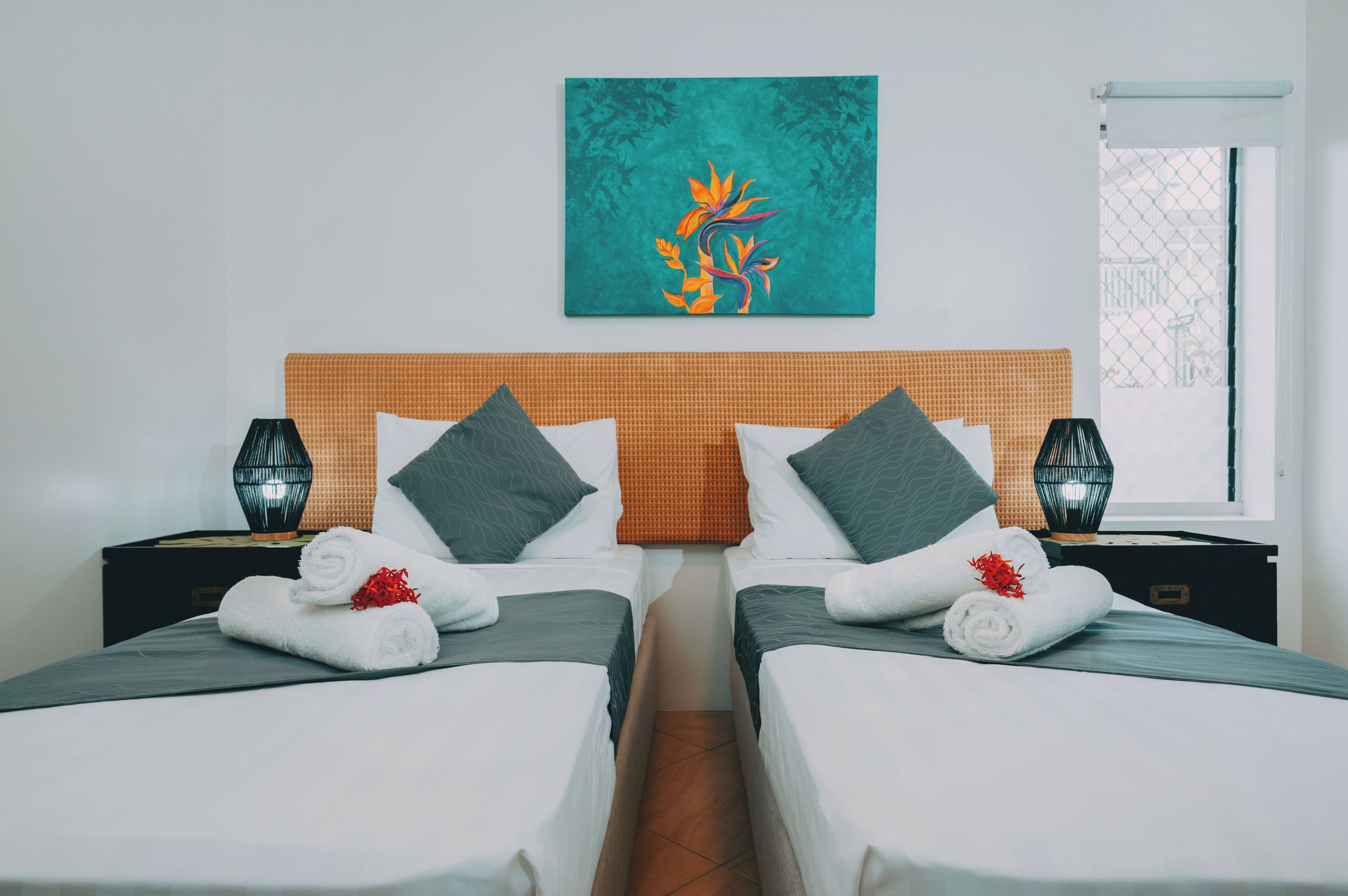 Camera d'albergo con due letti, una testiera in intreccio e un quadro appeso sopra.