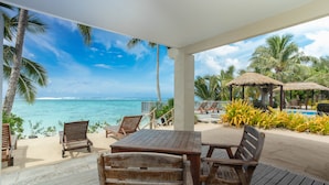 A wooden deck with a table and chairs, overlooking a beach with palm trees and a clear blue sky. - Moana Sands Villas & Apartments (Rarotonga)