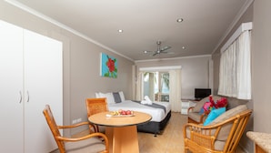 A hotel room with a bed, a dining table with chairs, a TV, and a balcony with curtains. - Moana Sands Villas & Apartments (Rarotonga)