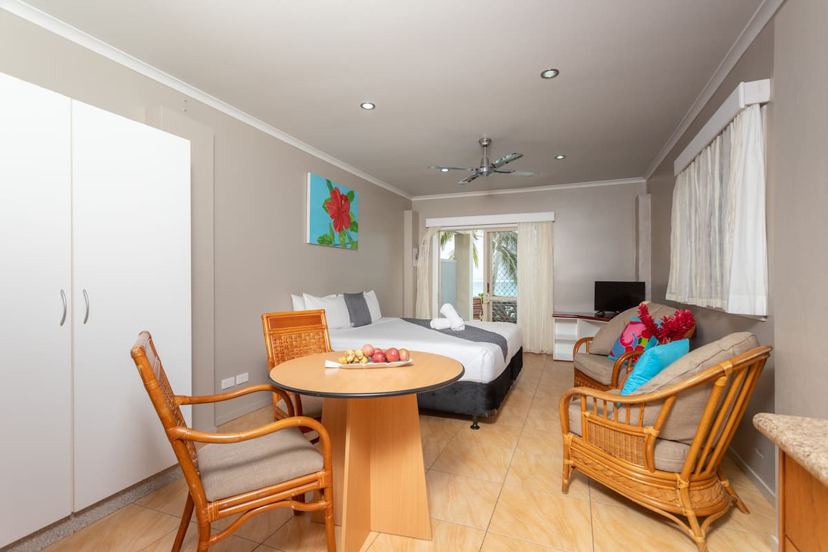 A hotel room with a bed, a dining table with chairs, a TV, and a balcony with curtains.
