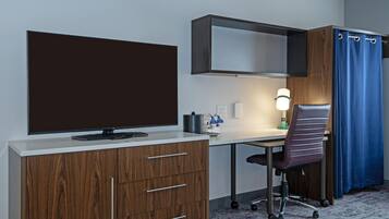 A hotel room with a flat-screen TV, wooden cabinet, desk, chair, and a shower curtain.