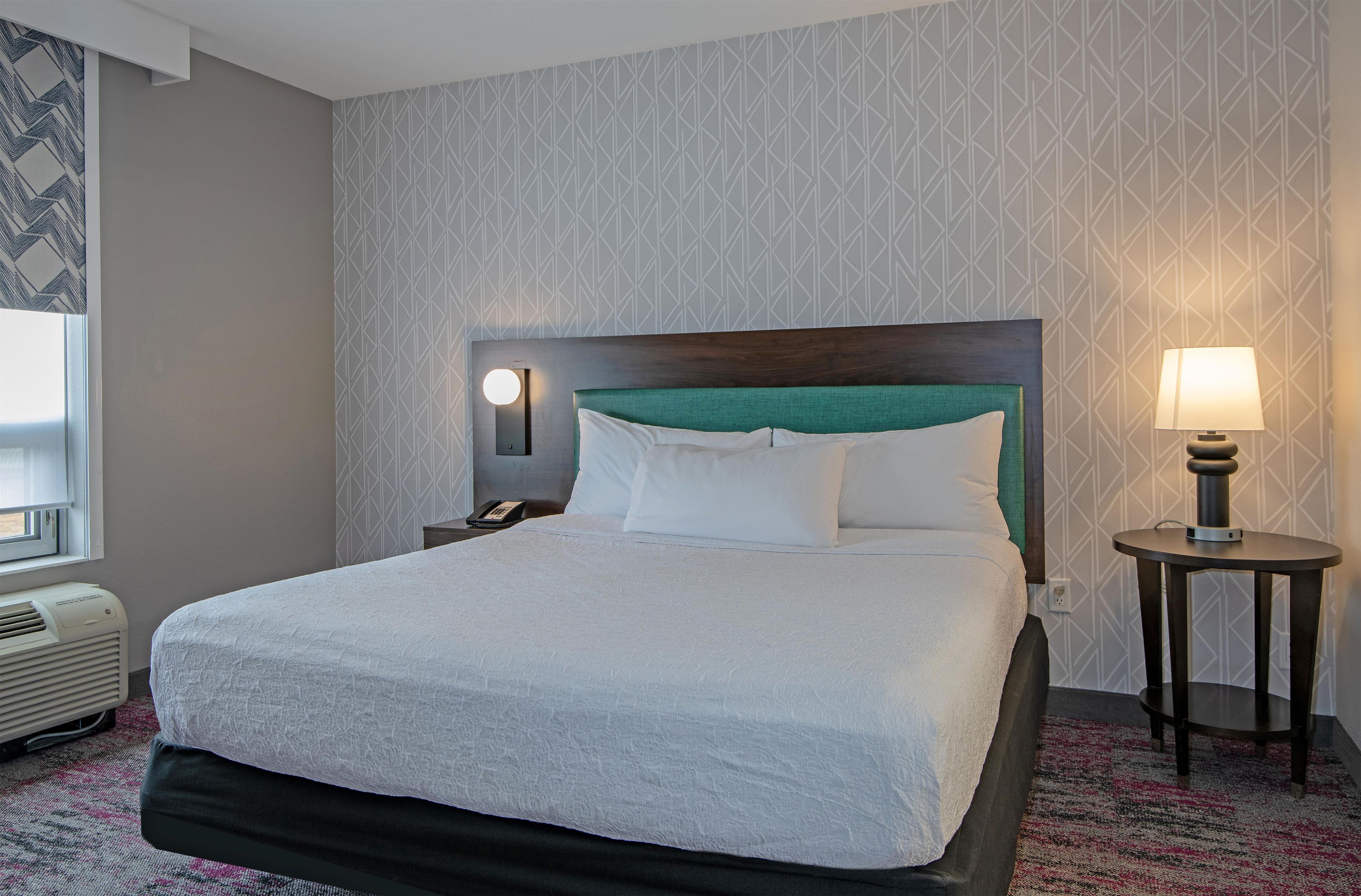 Une chambre d’hôtel avec un lit, une table de chevet, une lampe et un mur orné d’un motif géométrique.