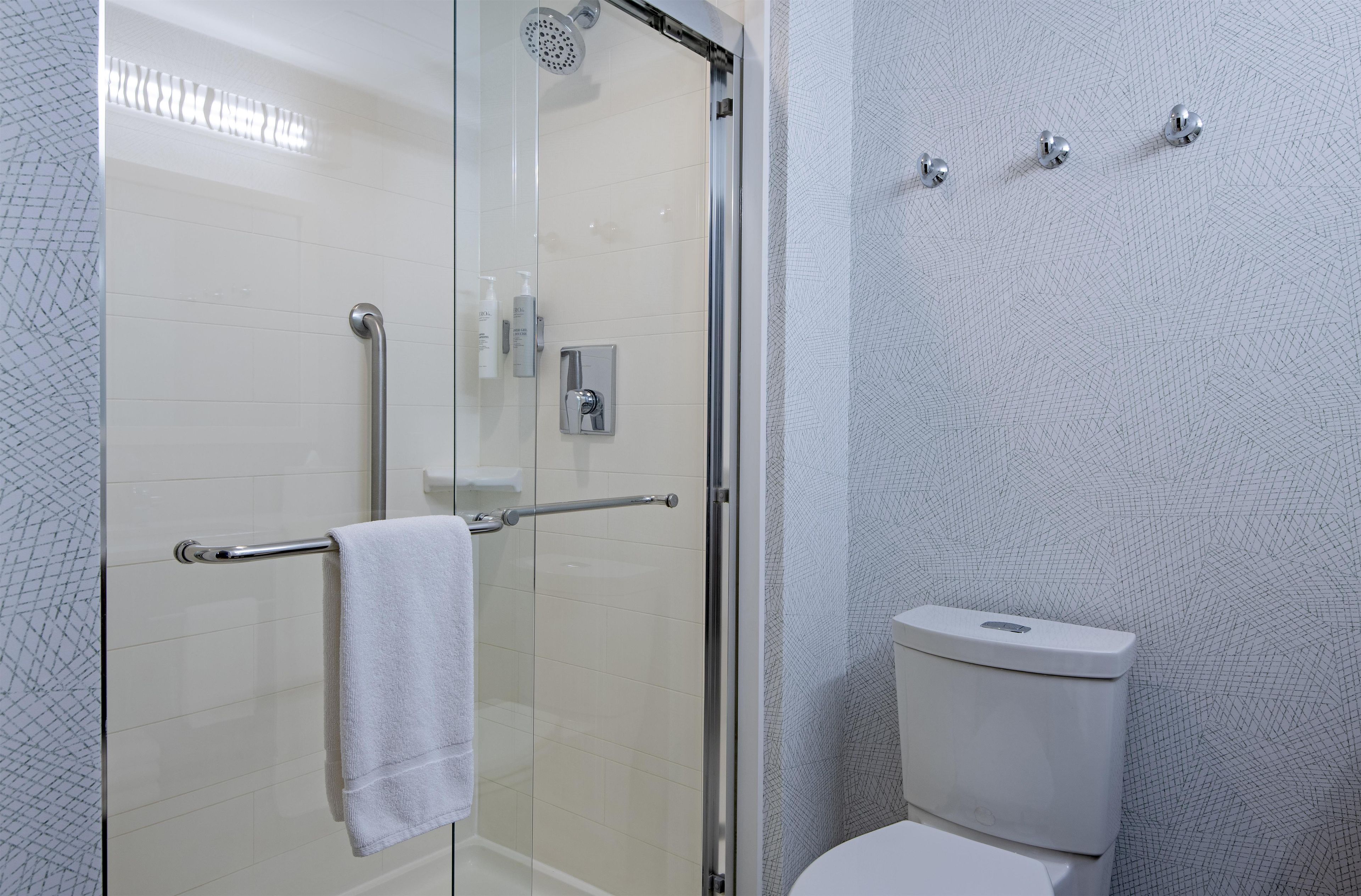 Une salle de bain avec une douche à parois de verre, des toilettes blanches et un porte-serviettes.