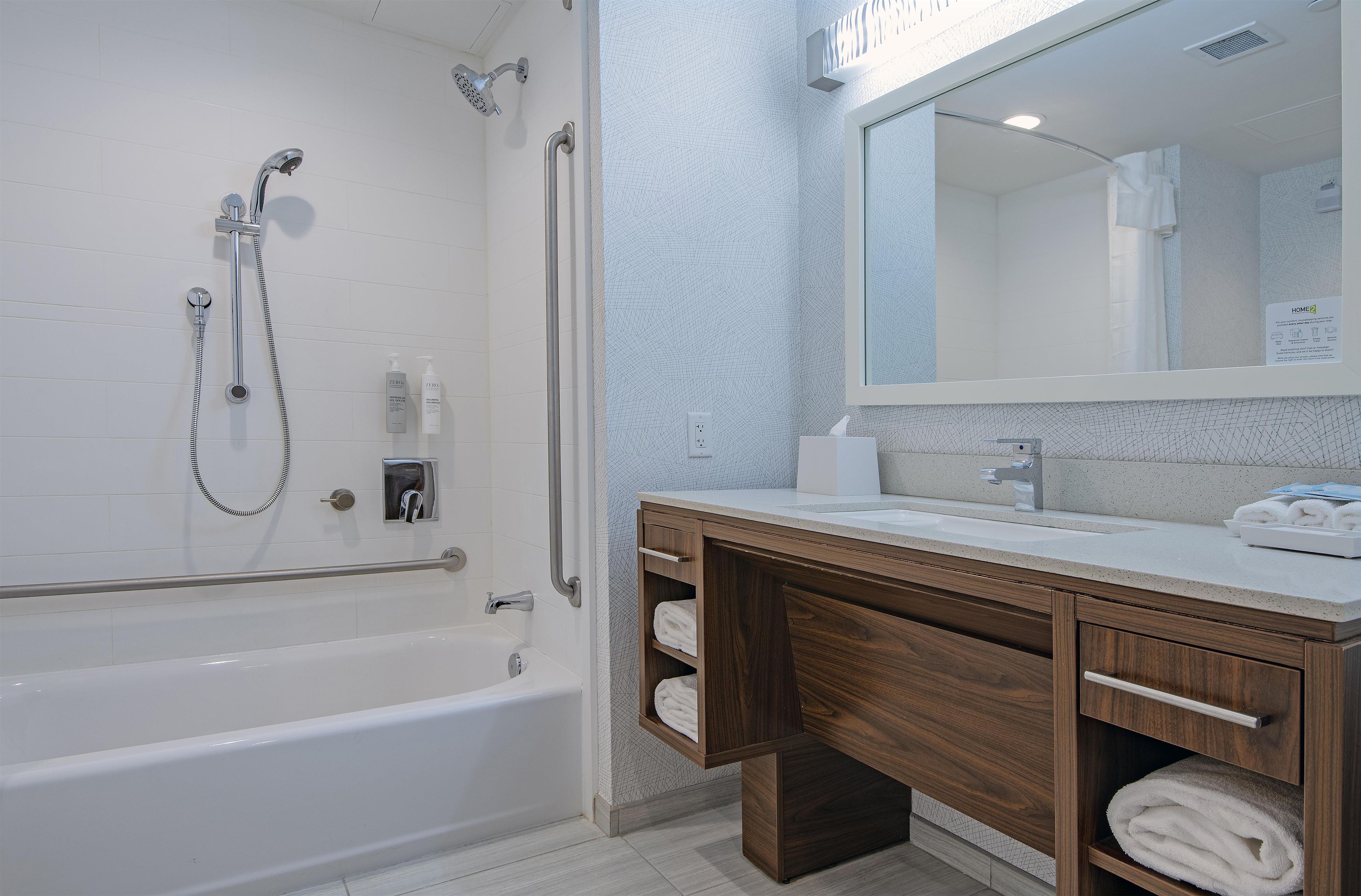 A modern bathroom with a bathtub, a shower, a vanity with a mirror, and a towel rack.