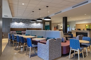 A modern restaurant with a central seating area, individual tables, and a counter. - Home2 Suites by Hilton West Edmonton, Alberta, Canada (Edmonton)