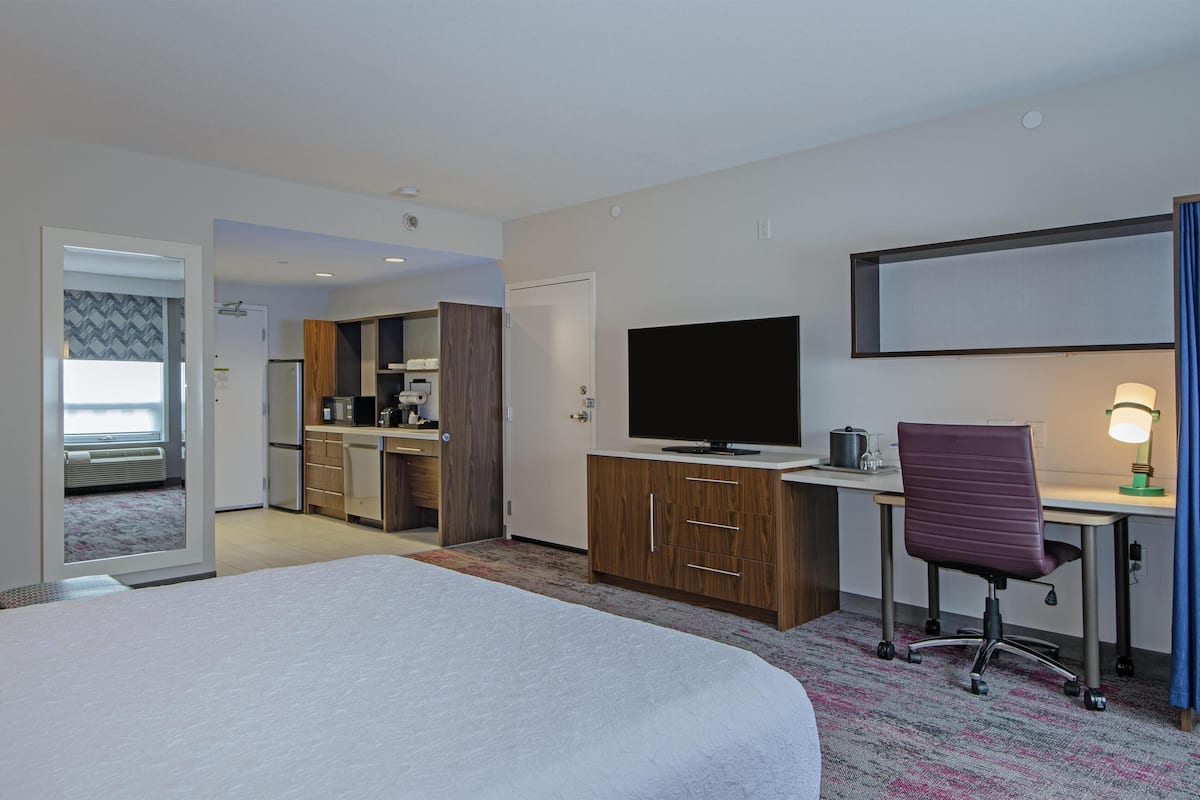 A hotel room with a bed, a desk with a computer, a television, and a kitchenette.