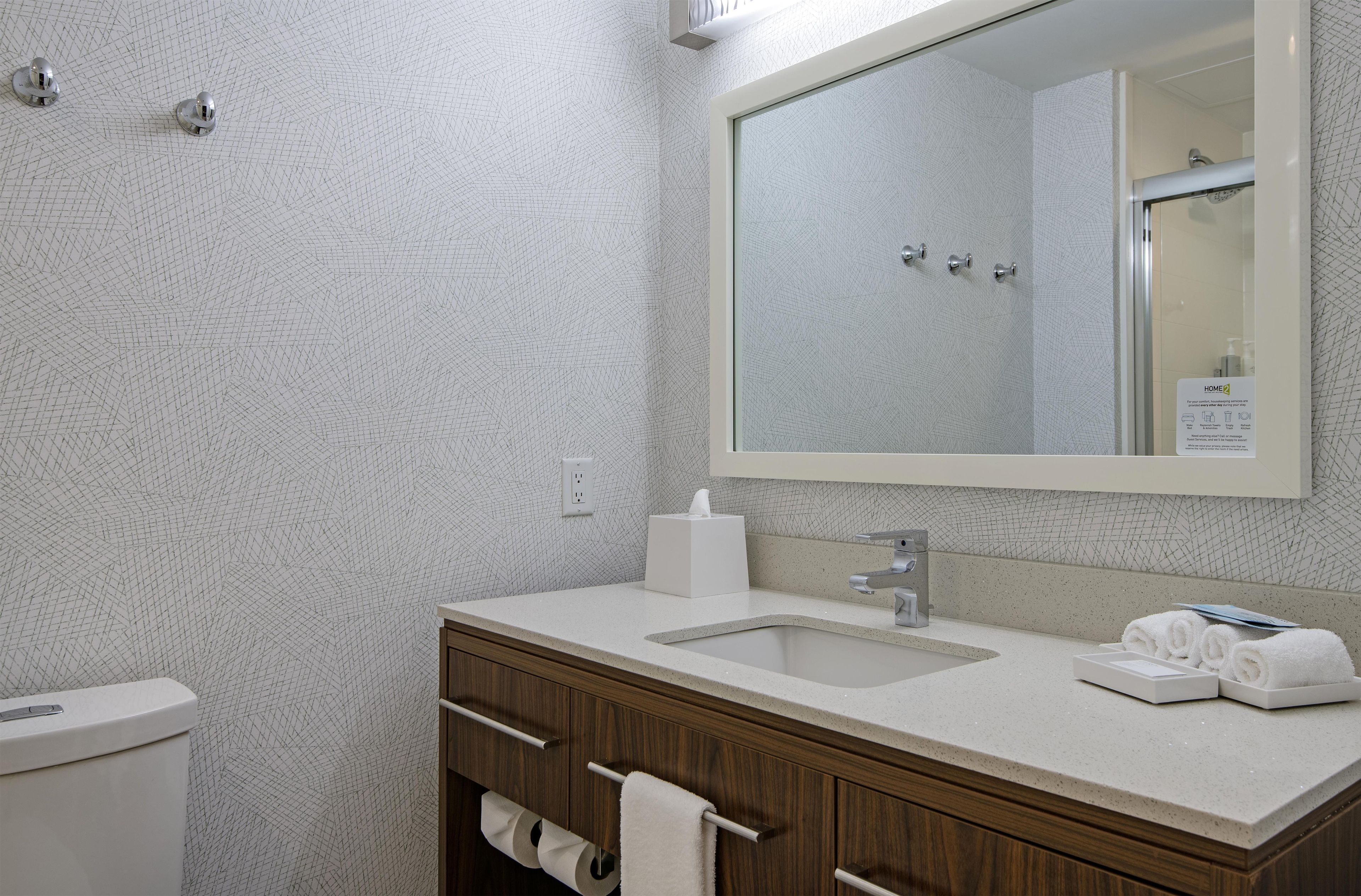 A bathroom with a white textured wall, a large mirror, a sink, a toilet, and a wooden vanity with a towel rack.