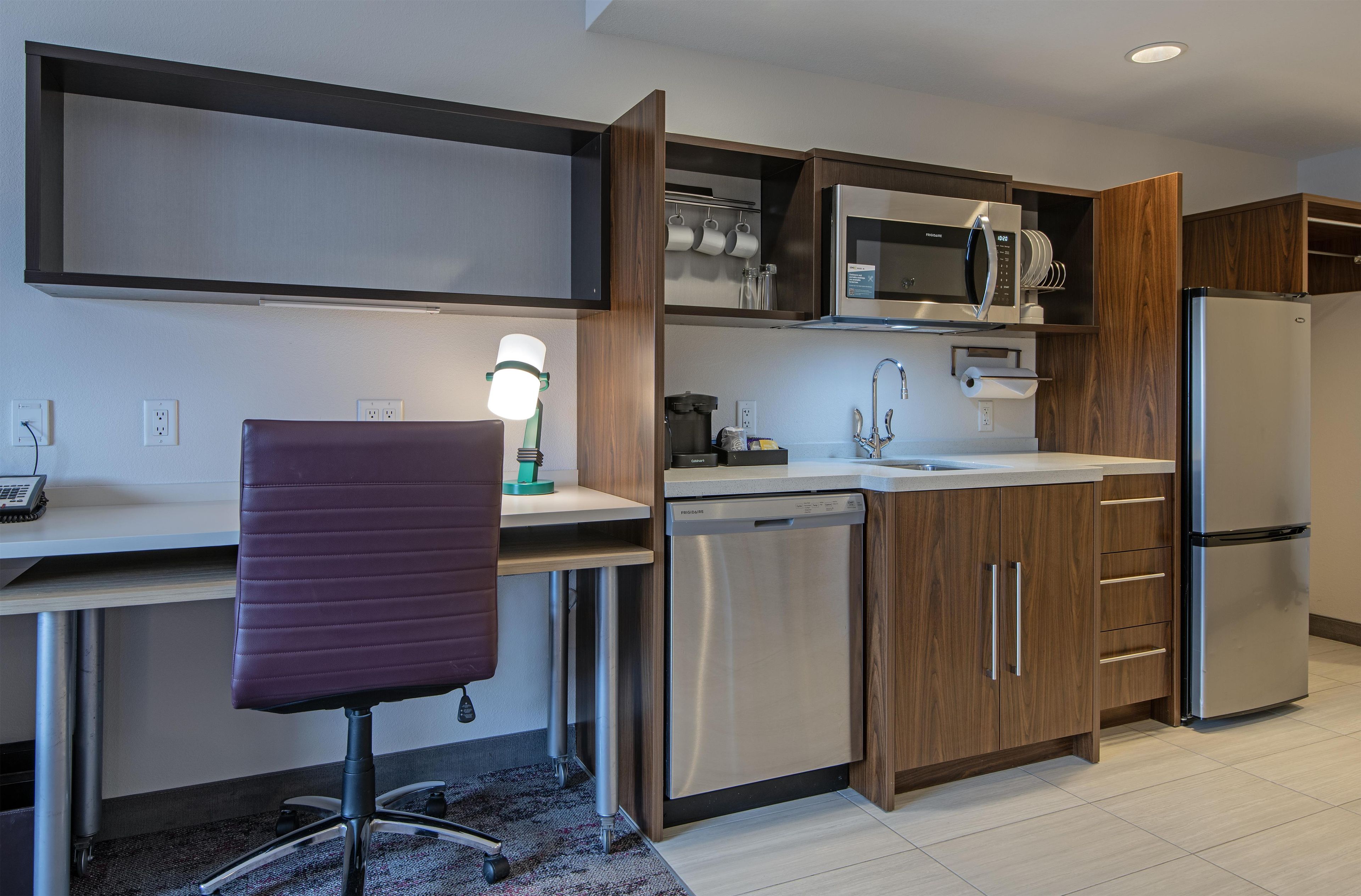 A modern kitchen with built-in appliances, a dining area with a chair, and a desk with a lamp.