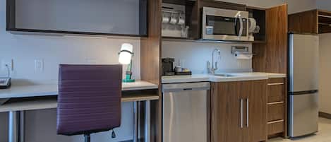 Una cocina moderna con electrodomésticos integrados, un comedor con una silla y un escritorio con lámpara.