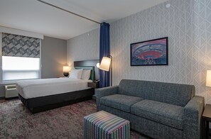 Habitación de hotel con cama, sofá, pared estampada, una obra de arte enmarcada y ventana con cortinas.