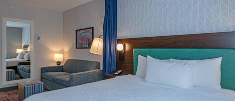 A hotel room with a large bed, a chair, a bedside table with a lamp, a phone, and a mirror.