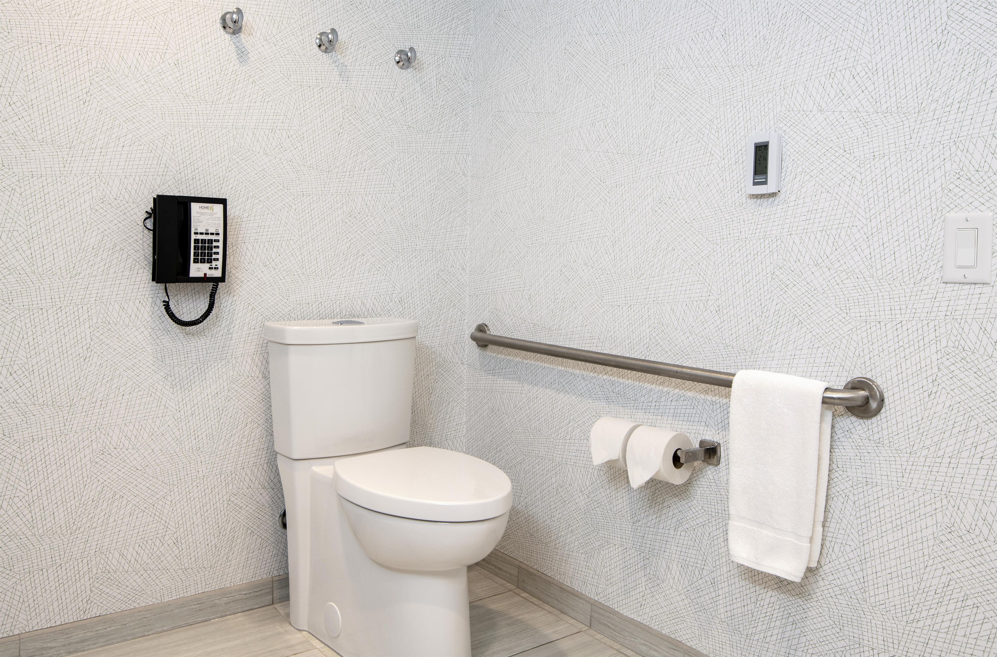 A bathroom with a toilet, a hand sanitizer dispenser, a towel rack, and a paper towel dispenser.
