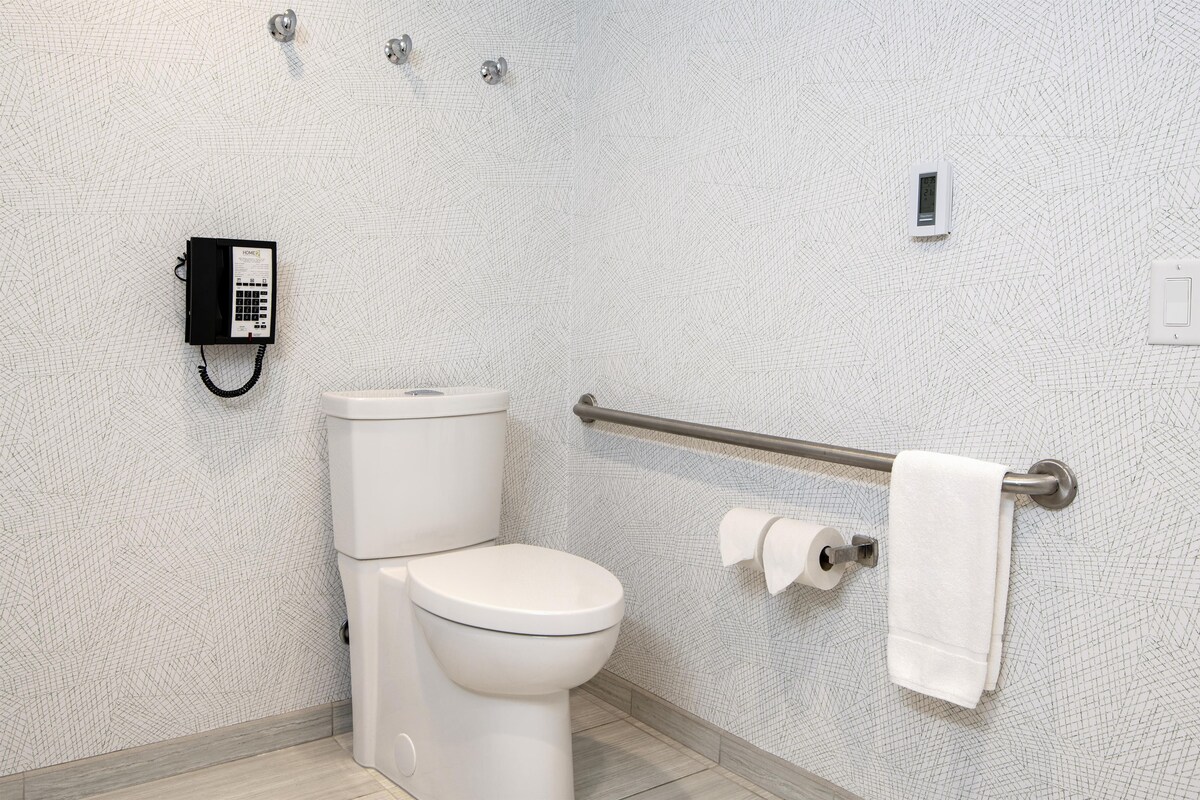 Un baño con inodoro, dispensador de gel antibacterial, toallero y dispensador de toallas de papel.