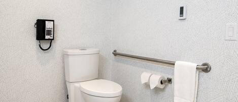 A bathroom with a toilet, a hand sanitizer dispenser, a towel rack, and a paper towel dispenser.