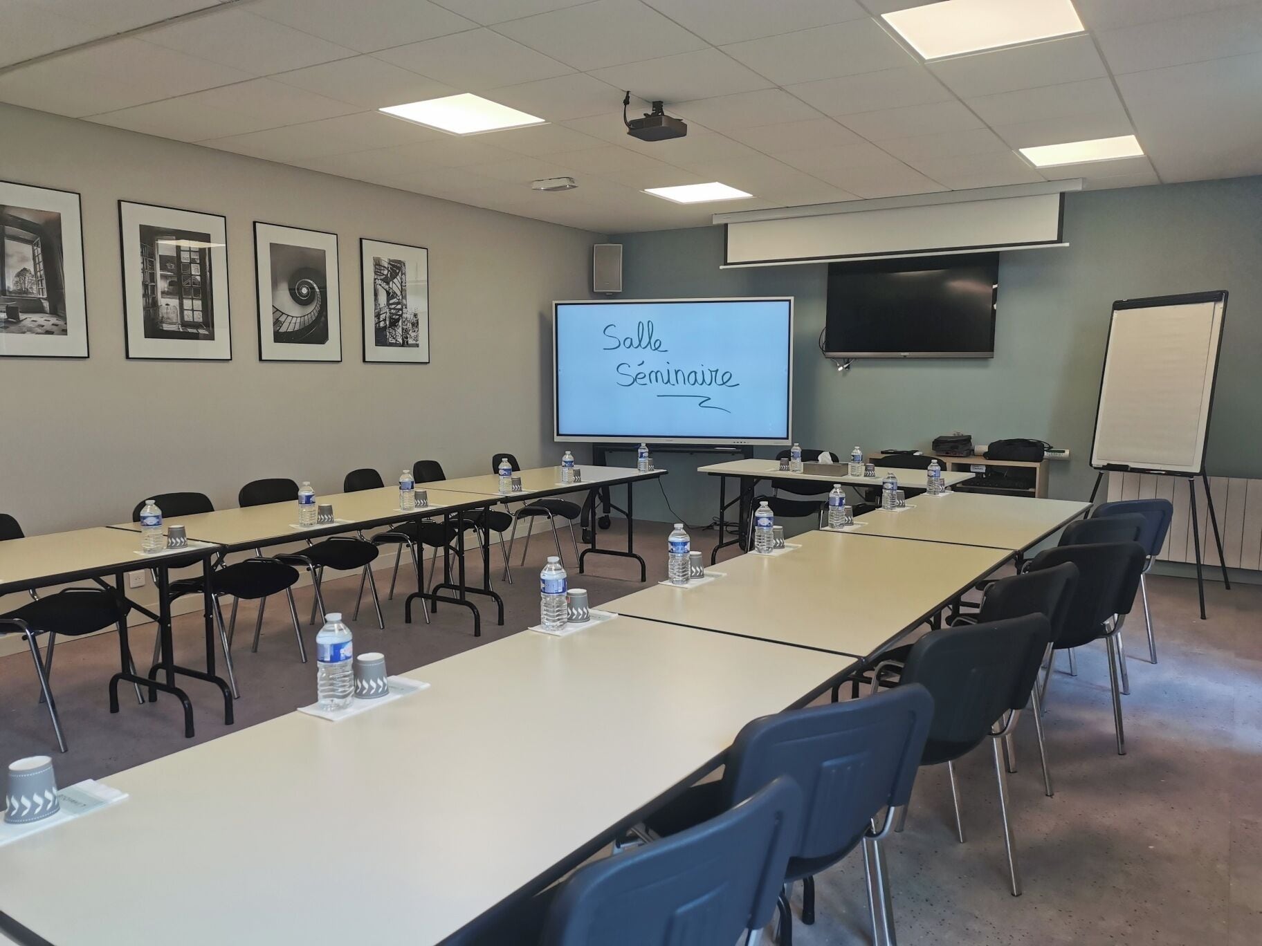 A conference room with long tables, chairs, a projector screen, and a whiteboard.