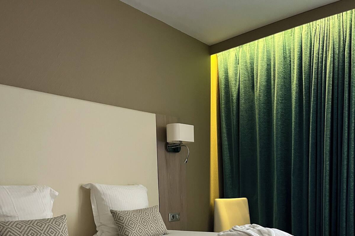A neatly made bed with pillows, a bedside lamp, and a window with curtains.