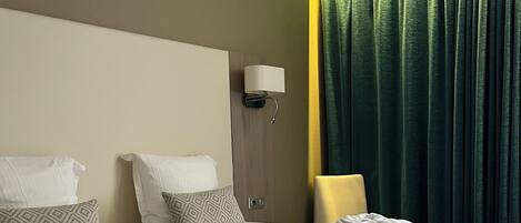 A neatly made bed with pillows, a bedside lamp, and a window with curtains.