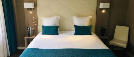 Habitación de hotel con una cama grande, dos almohadas, una mesita de noche con una lámpara y una silla.
