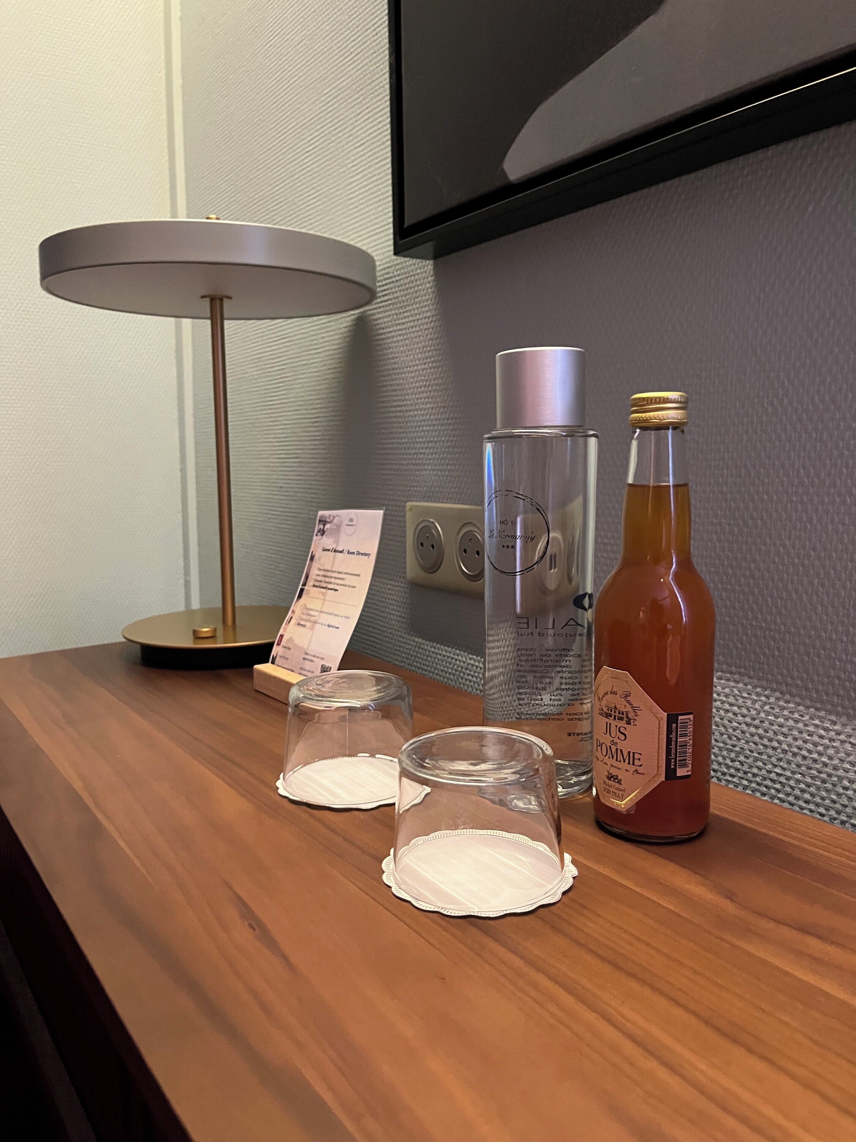 Una barra de madera con una lámpara, una botella de jugo de manzana, dos vasos vacíos y un letrero.