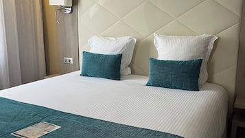 A hotel room with a large bed, two pillows, a bedside lamp, and a window with curtains.